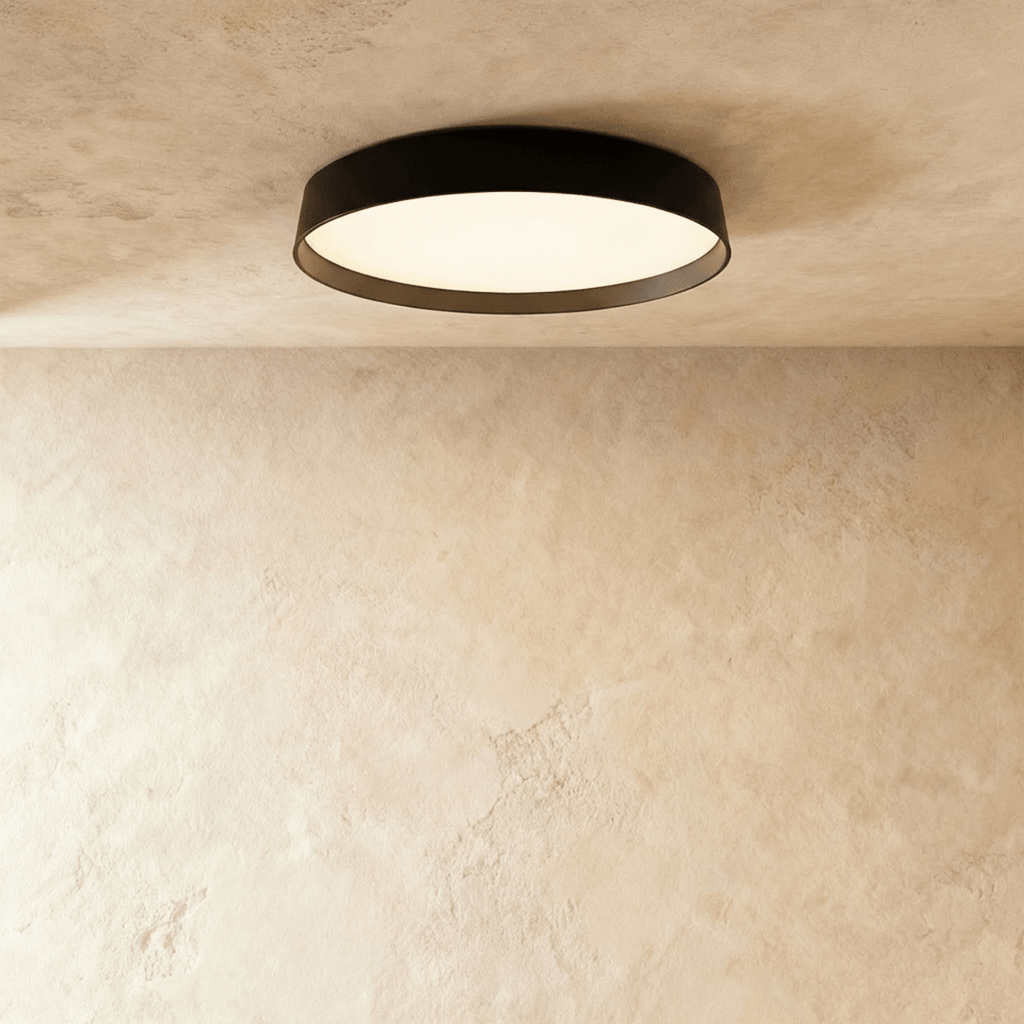 Clérachic flat round ceiling light with a black rim and a diffused white panel glowing softly, mounted on a plaster ceiling.
