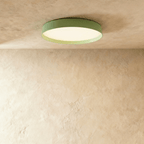 Clérachic flat round ceiling light in soft sage green with a lit white diffuser, fixed flush to a textured plaster ceiling.