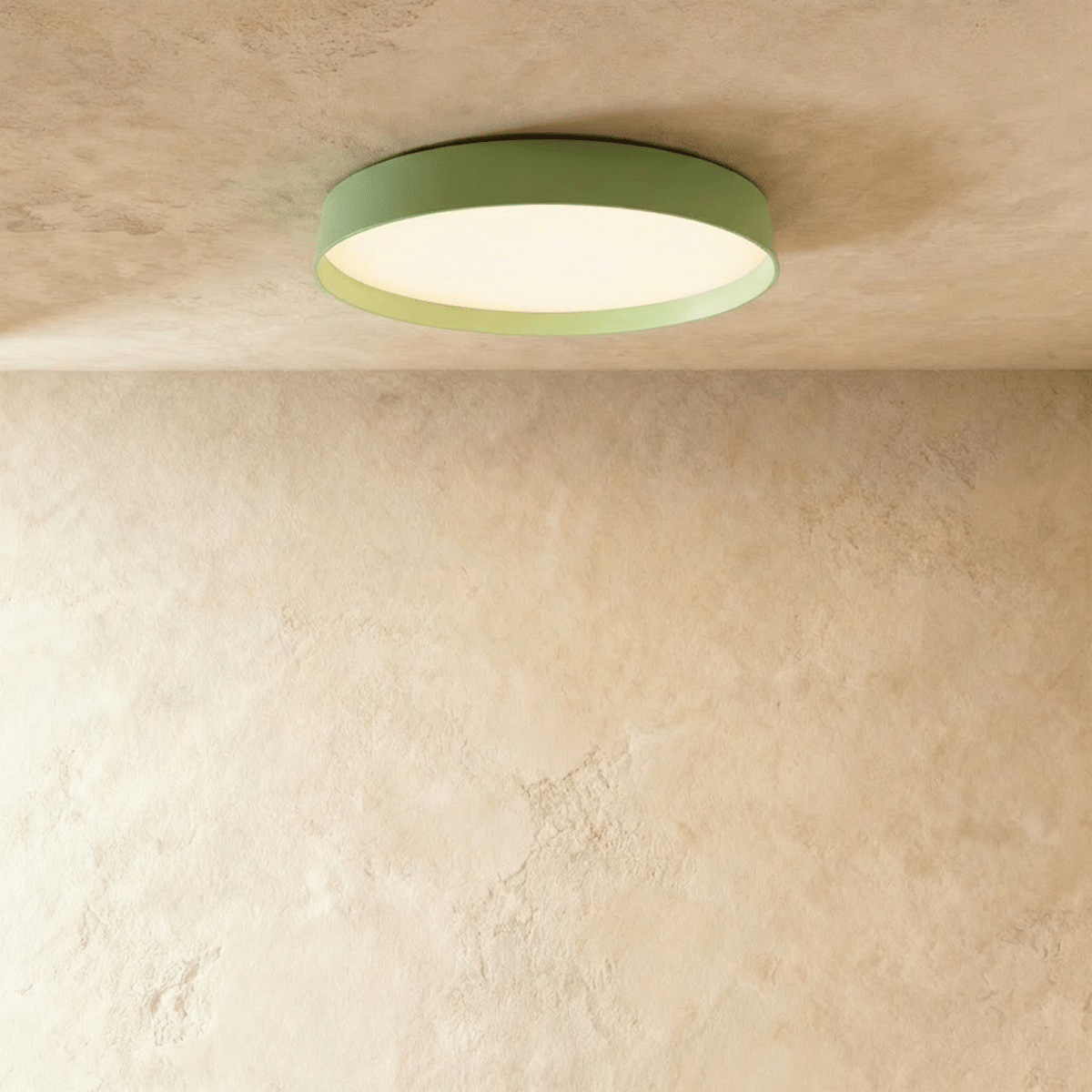 Clérachic flat round ceiling light in soft sage green with a lit white diffuser, fixed flush to a textured plaster ceiling.