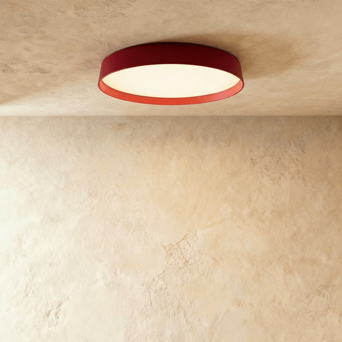 Clérachic flat round ceiling light with a deep red rim and orange inner edge, its diffuser glowing on a plaster ceiling.