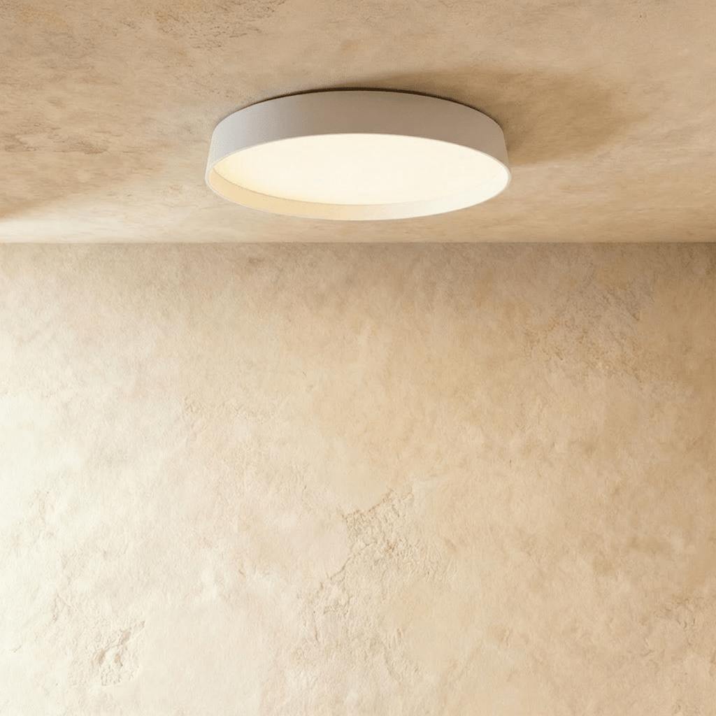 Clérachic flat round ceiling light in white with a softly lit diffuser, seen from below on a limewash plaster ceiling.