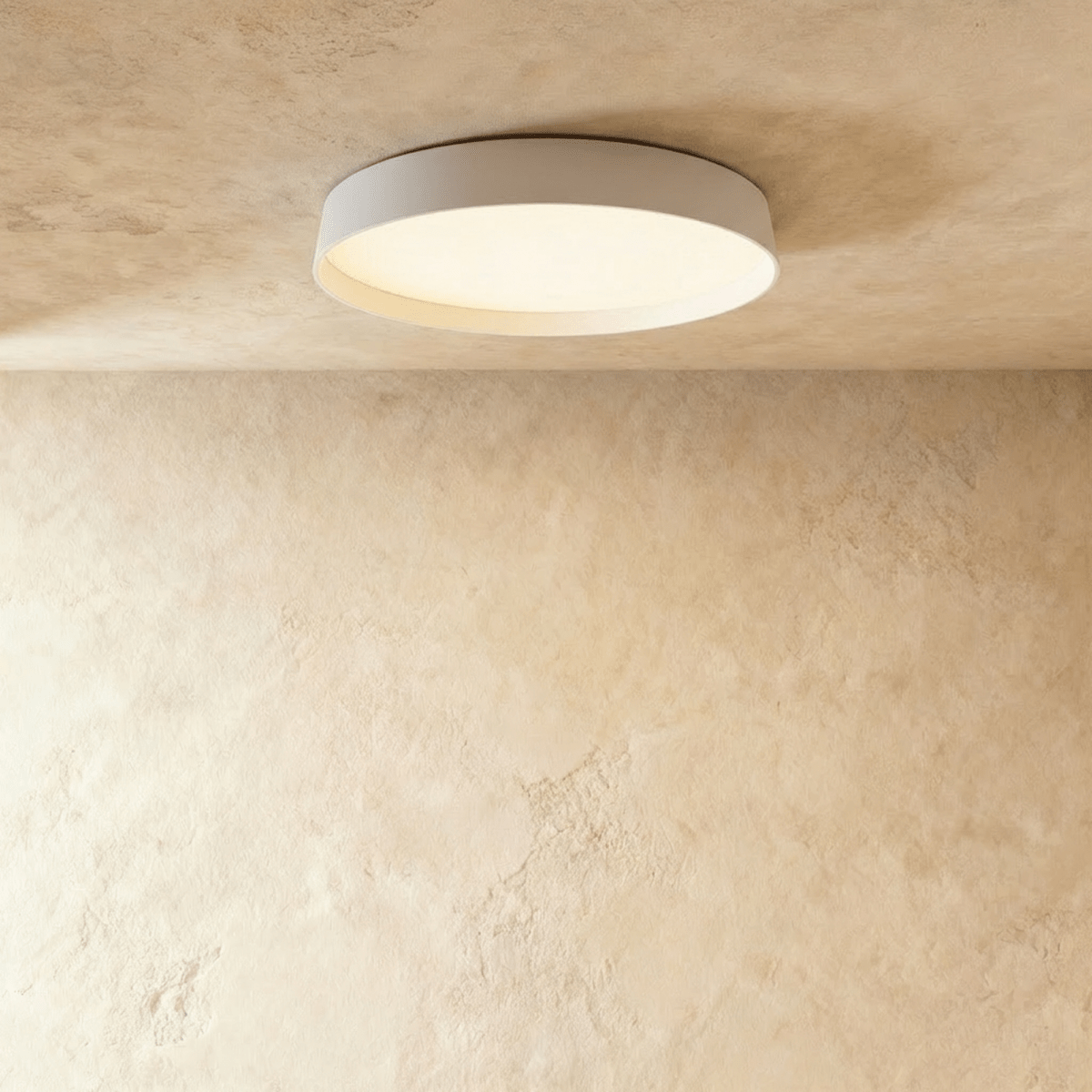 Clérachic flat round ceiling light in white with a softly lit diffuser, seen from below on a limewash plaster ceiling.