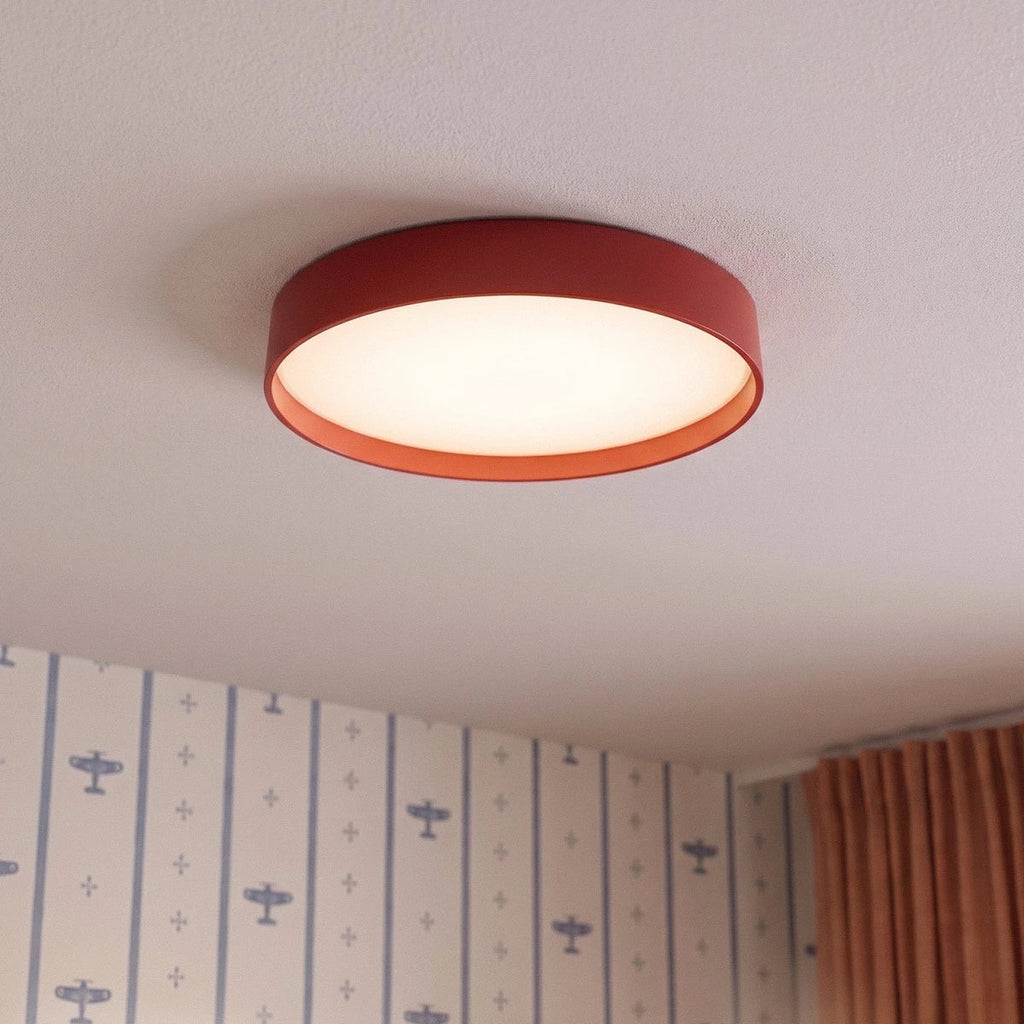 Close view of a Clérachic red round ceiling light with a lit white diffuser, beside aeroplane-print wallpaper and rust curtains.