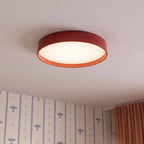 Close view of a Clérachic red round ceiling light with a lit white diffuser, beside aeroplane-print wallpaper and rust curtains.