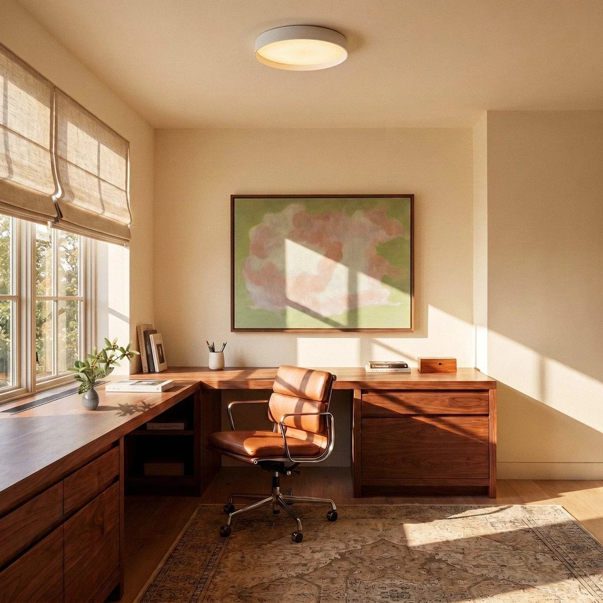 Clérachic white flush ceiling light over a walnut corner desk with a leather chair, in a sunlit study with a framed painting.