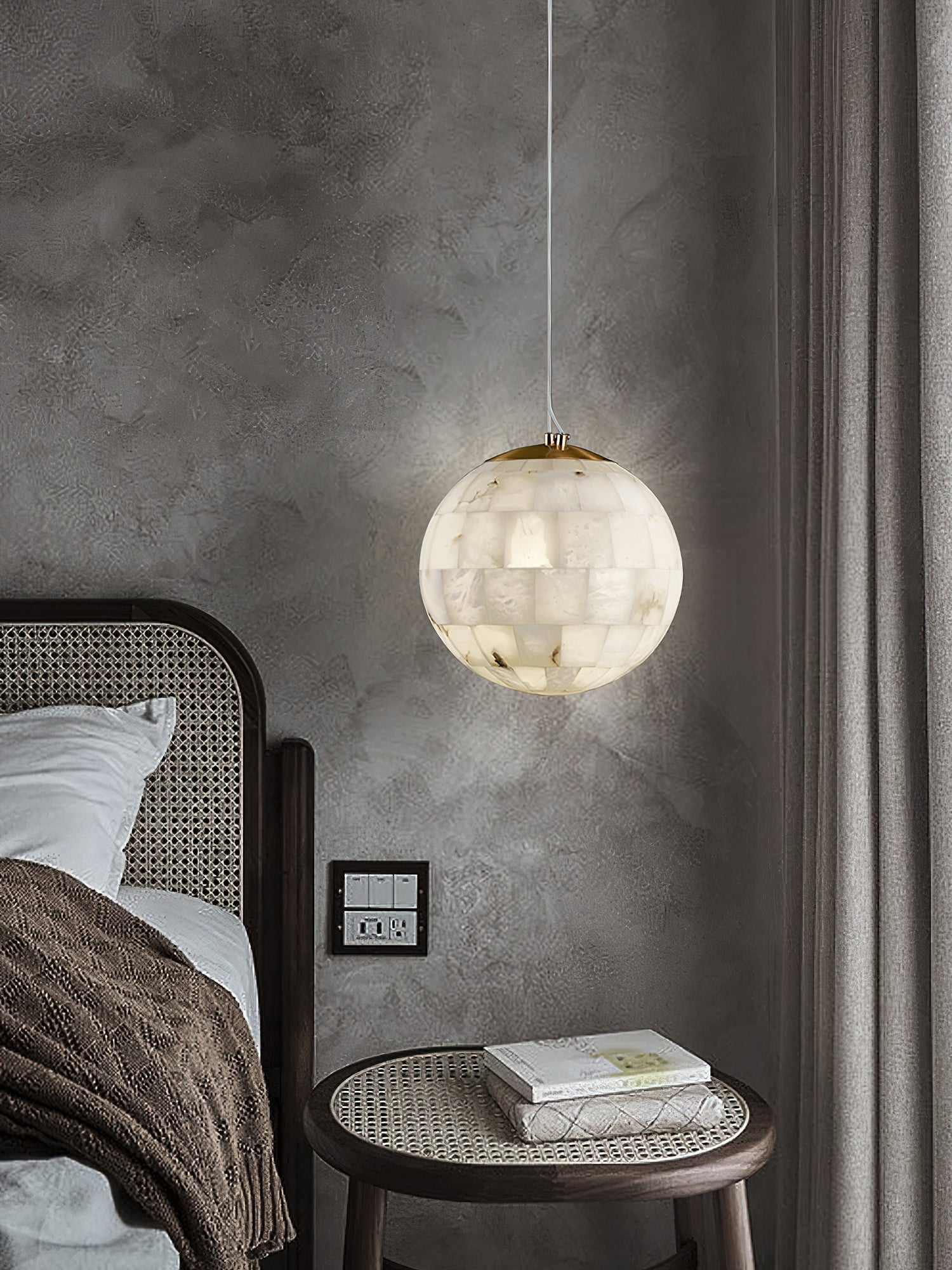 Clérachic globe pendant hanging in a dark plaster bedroom beside a cane headboard and round side table.