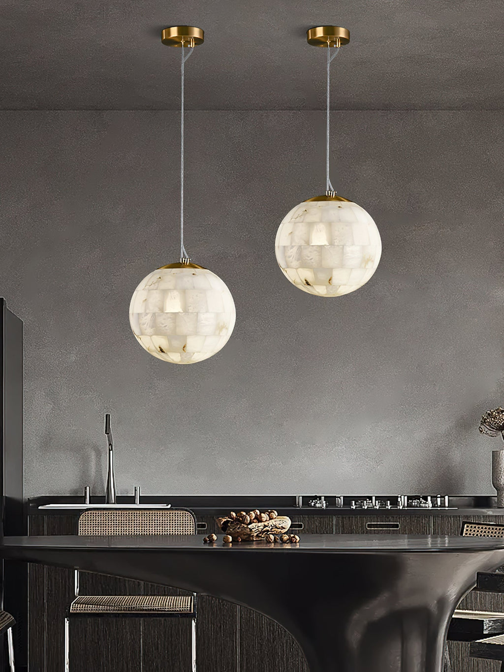 Two Clérachic alabaster pendants hung at staggered drops above a dark kitchen island.