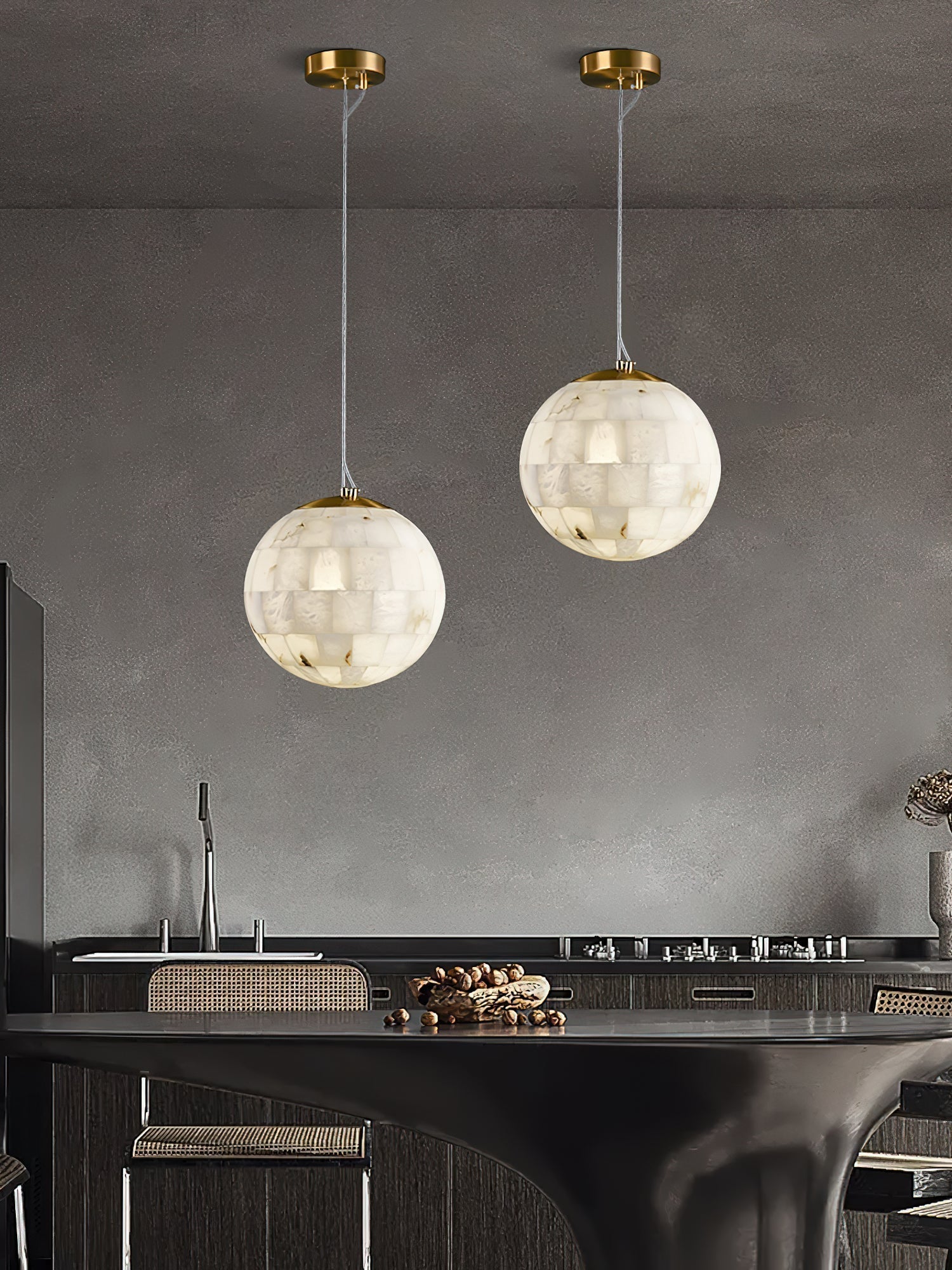 Two Clérachic alabaster pendants hung at staggered drops above a dark kitchen island.