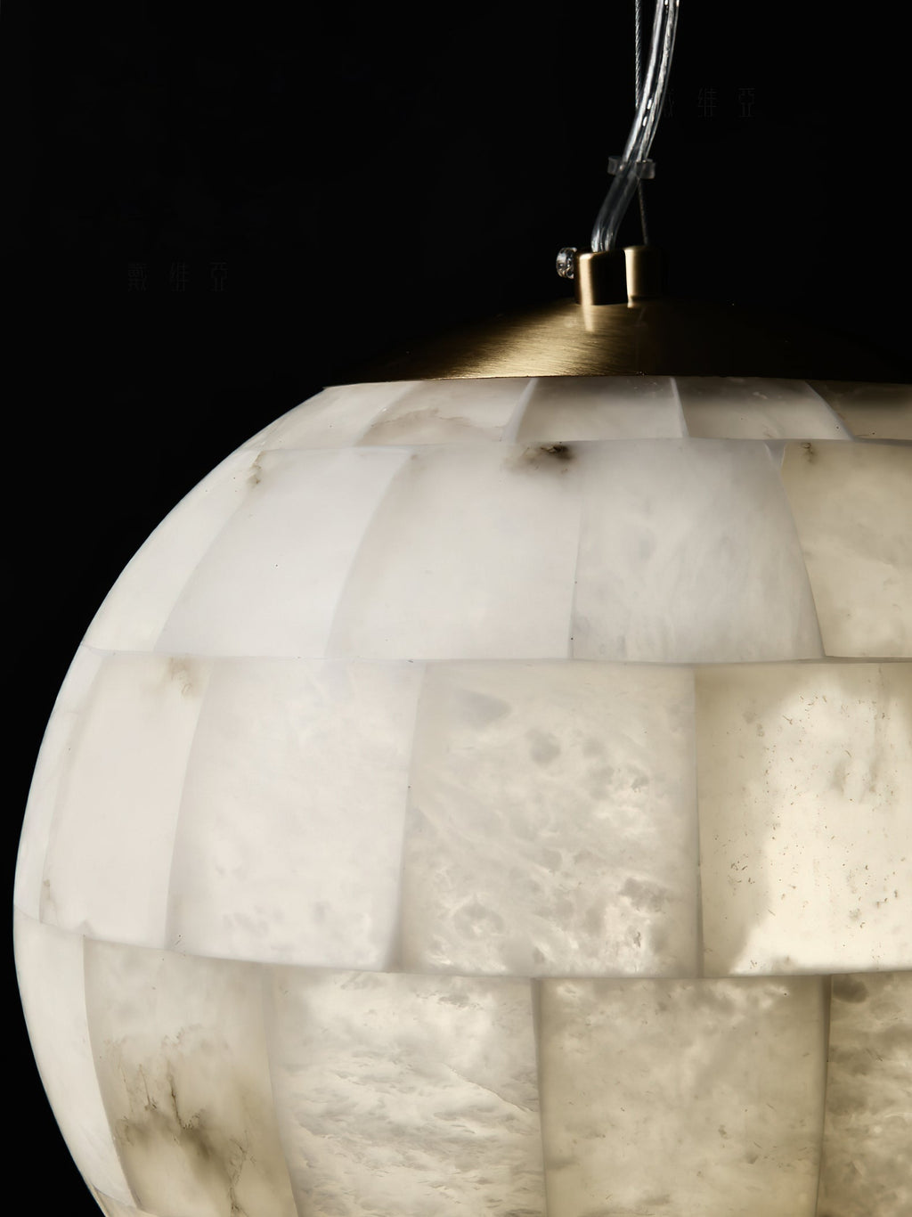 The Clérachic pendant's brass top collar and cable clamp seen close against the warm alabaster tiles.