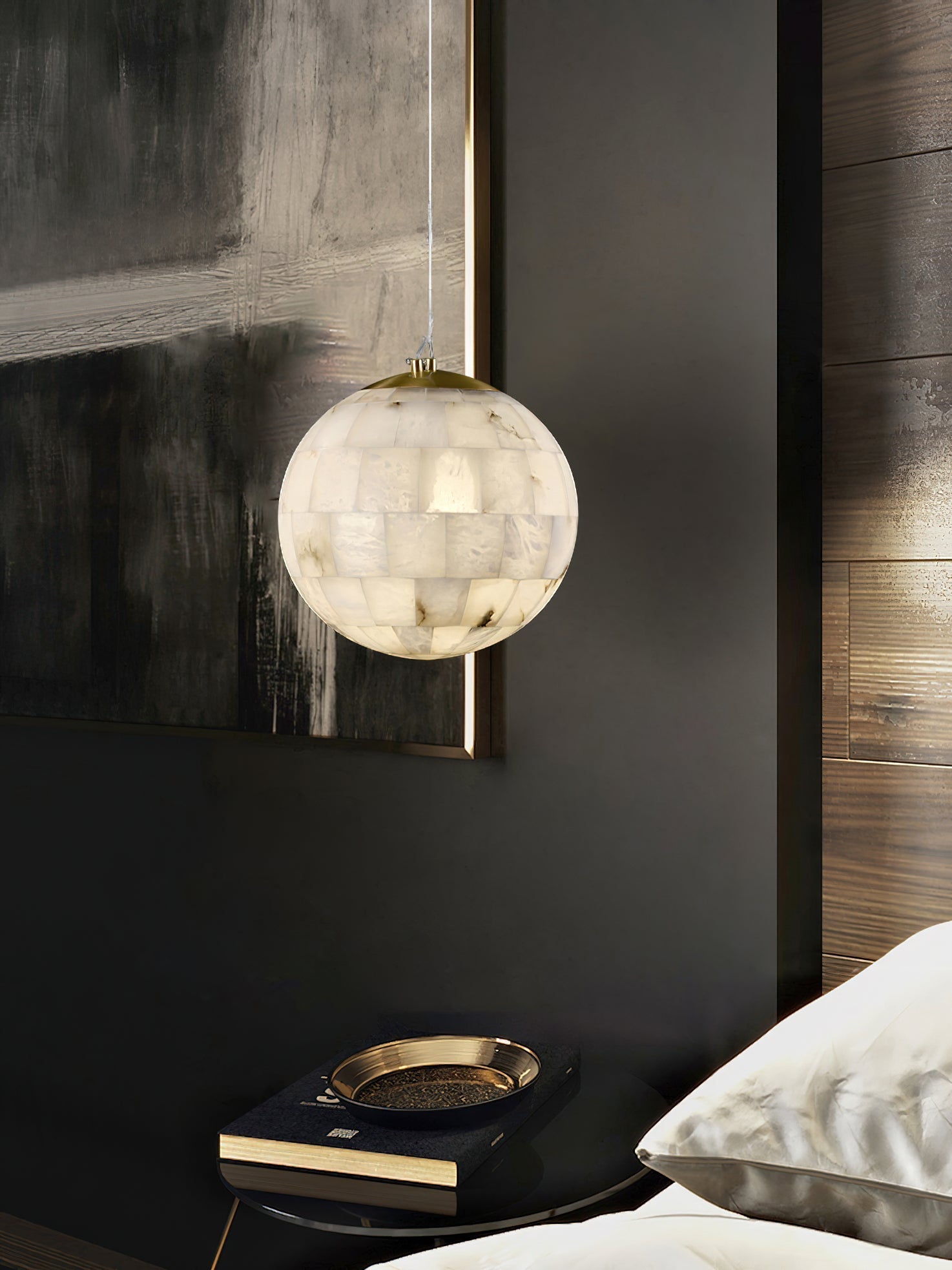 The Clérachic pendant lit in a dark bedroom, hanging beside moody artwork and a brass bedside tray.