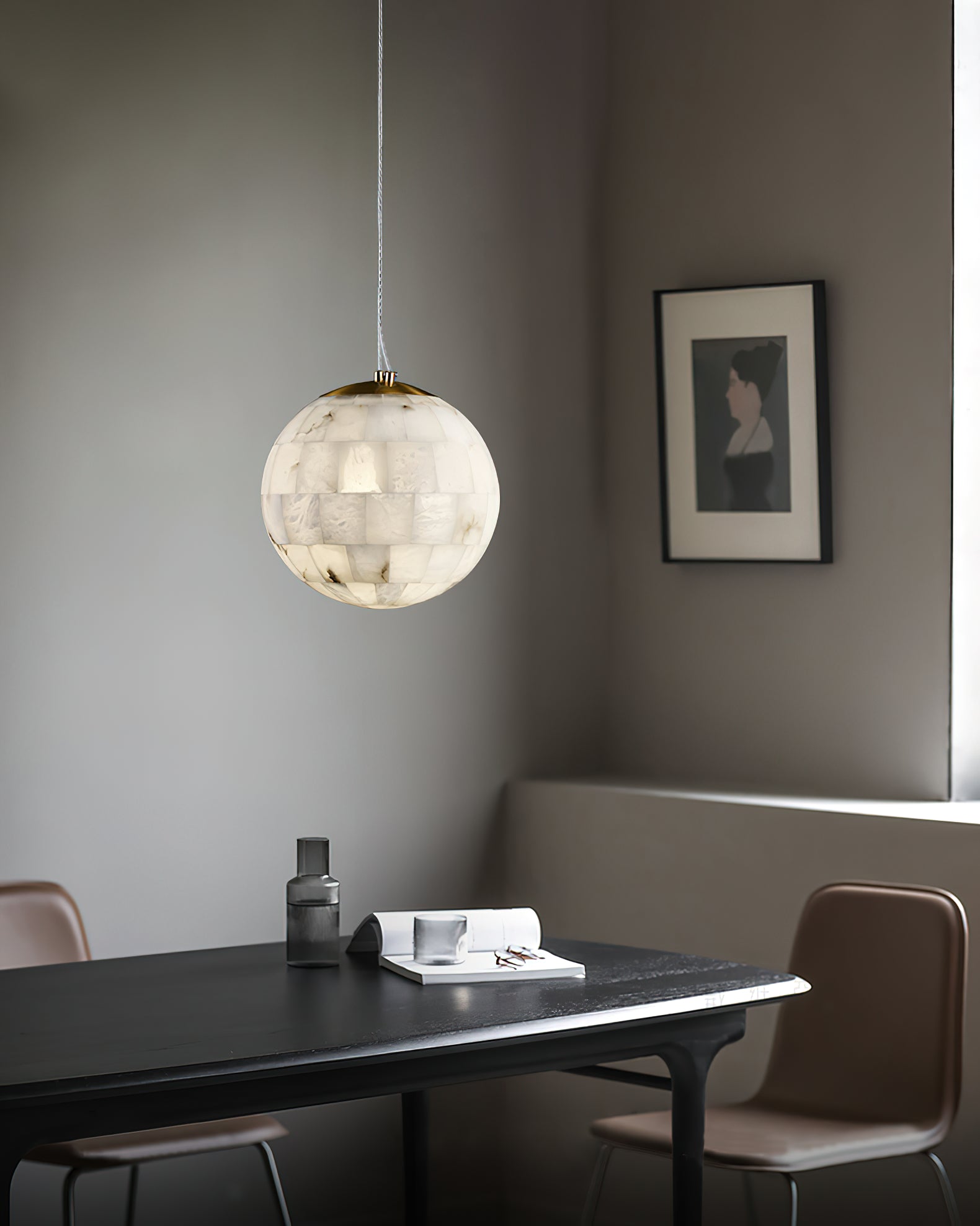 Clérachic globe pendant over a black dining table with tan chairs and a framed portrait behind.