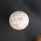 The Clérachic alabaster pendant lit large against a charcoal wall, its soft shadow falling behind.