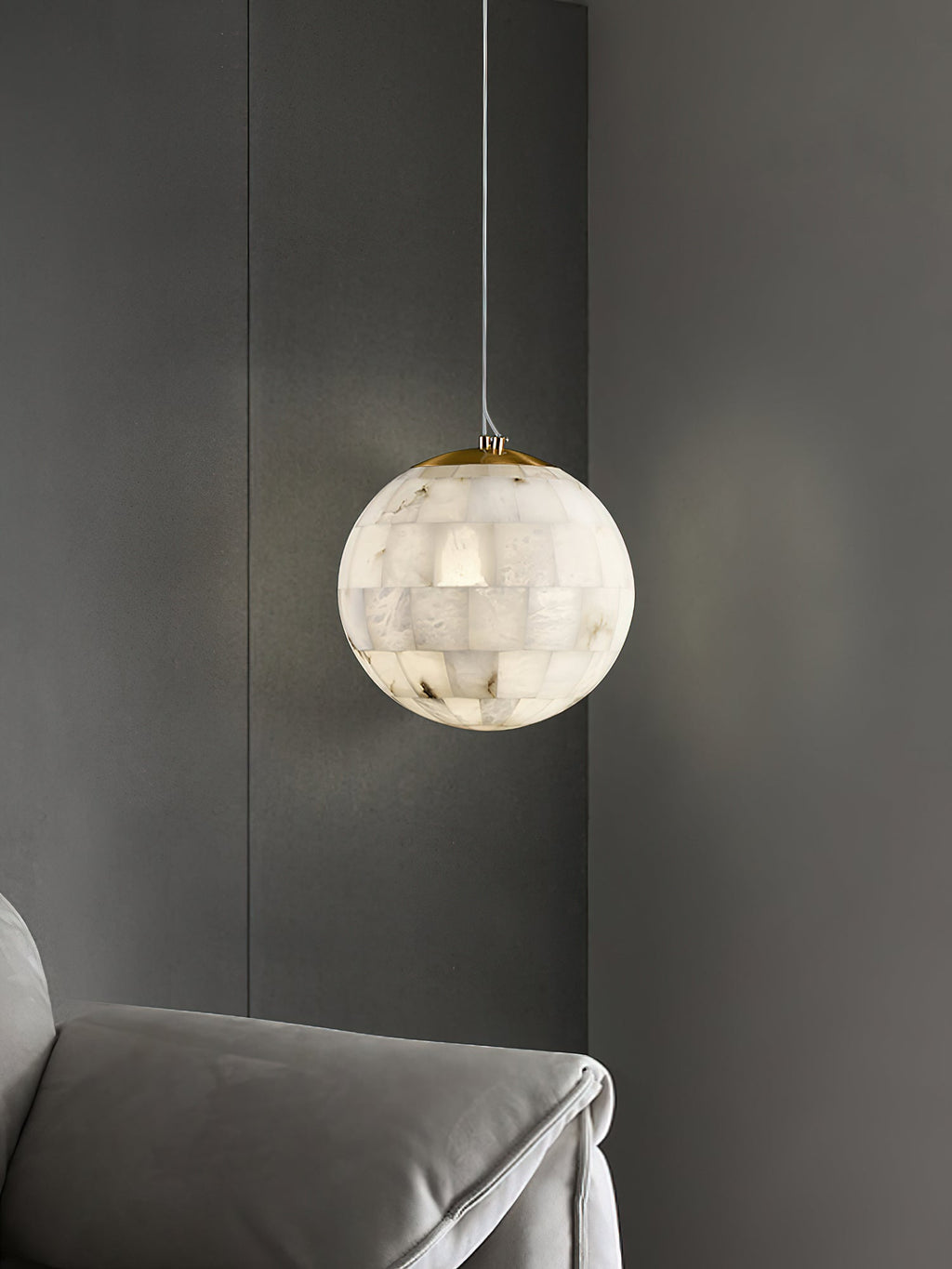 The Clérachic pendant lit beside a grey panelled wall, dropping past the arm of an upholstered sofa.