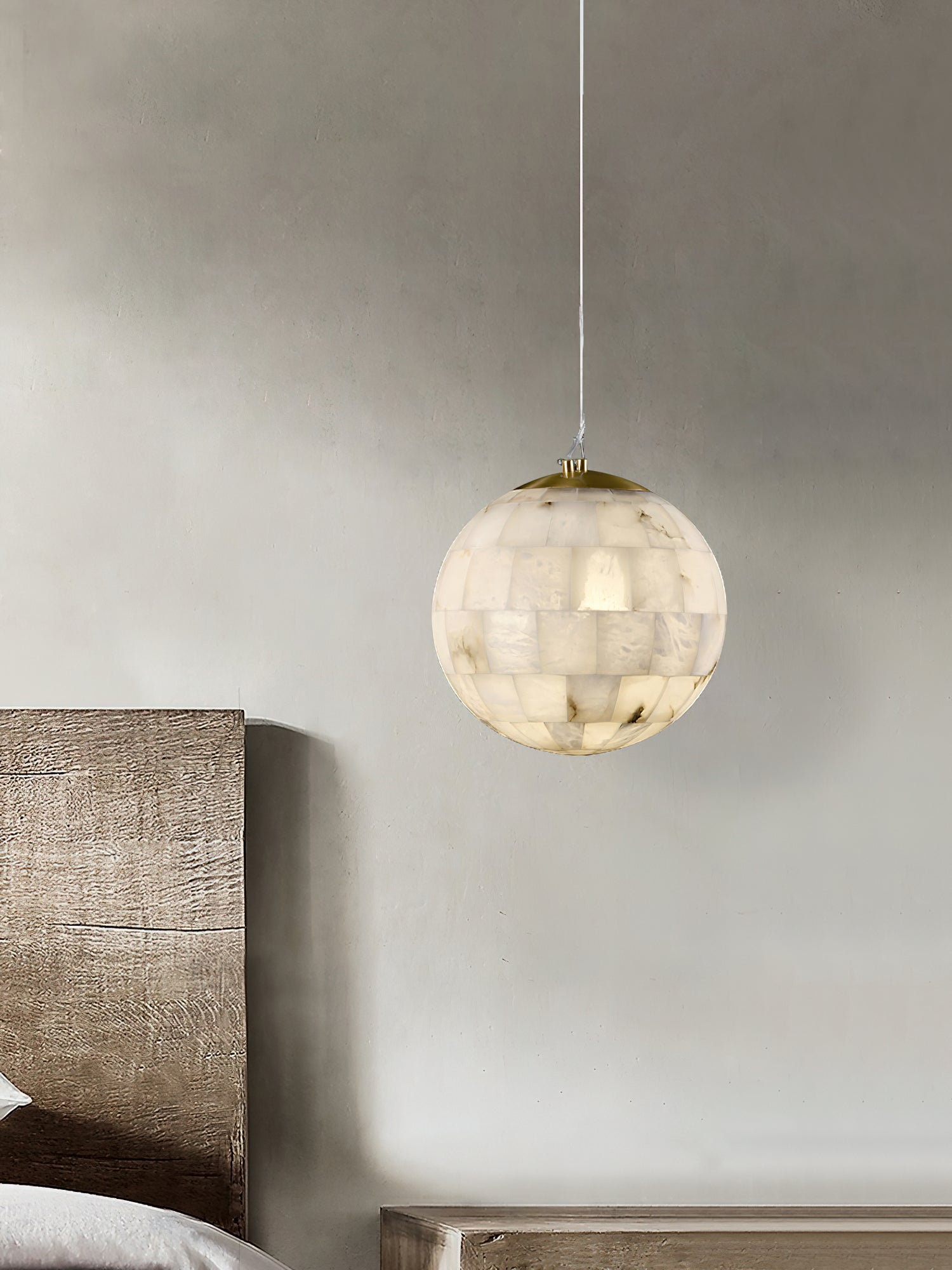 Clérachic alabaster pendant hanging over a bench beside a timber headboard in a soft plaster bedroom.