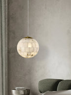 Clérachic pendant glowing on a plaster wall above a green sofa, ribbed curtains drawn to one side.
