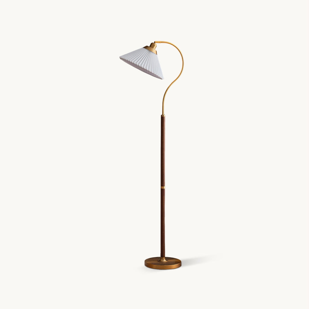 Floor lamp from Clérachic with a white pleated shade on a curved brass arm, a walnut stem and a round brass base, on white.