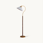 Floor lamp from Clérachic with a white pleated shade on a curved brass arm, a walnut stem and a round brass base, on white.