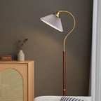 Close view of the white pleated shade and the walnut stem of this Clérachic floor lamp, beside a cane cabinet and a dried-flower vase.