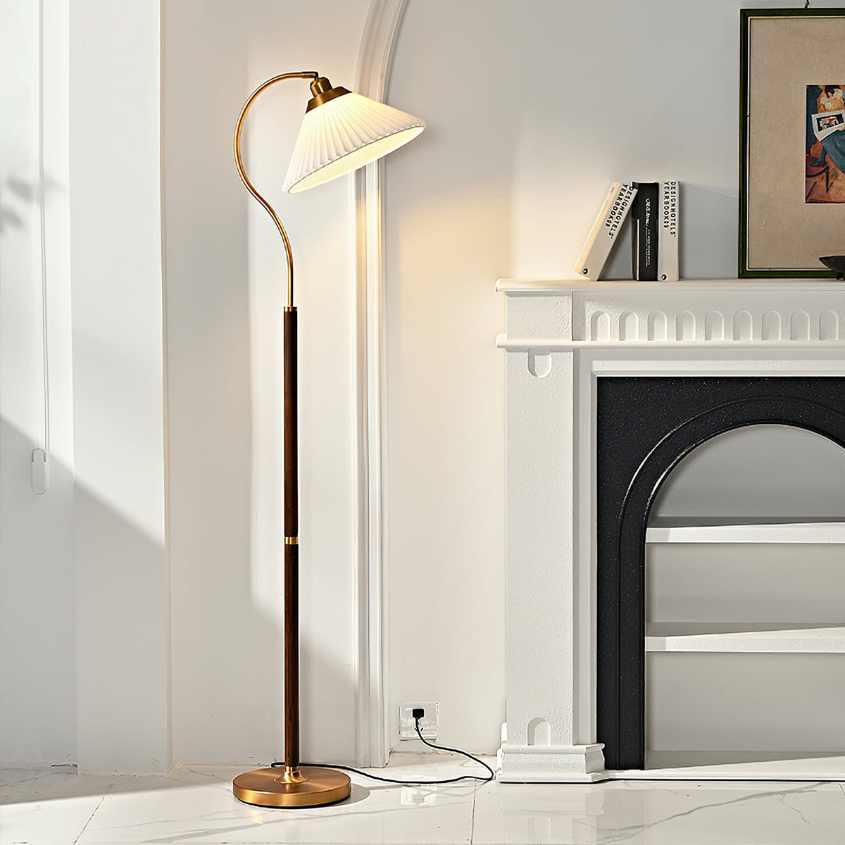 The white pleated shade of this Clérachic floor lamp is lit beside a white fireplace and a framed print, on a marble-look floor.
