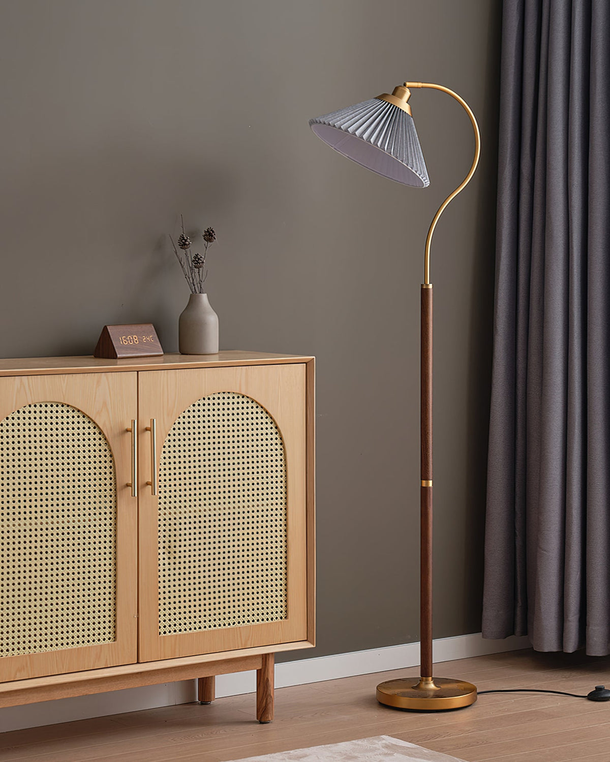 A Clérachic floor lamp with a grey pleated shade by the same cane cabinet and grey curtains, shown unlit.