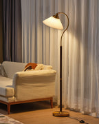 Warm light from this Clérachic floor lamp falls on sheer curtains and a cream sofa with an orange cushion.