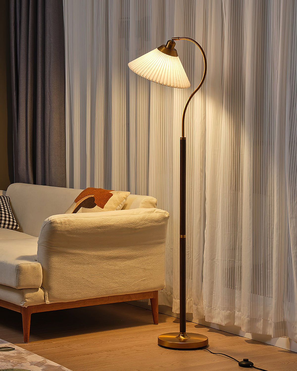 Warm light from this Clérachic floor lamp falls on sheer curtains and a cream sofa with an orange cushion.