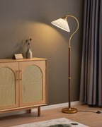 The Clérachic floor lamp with a white pleated shade, lit, throws a warm cone of light on the taupe wall above a cane cabinet.