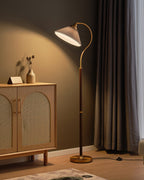 A lit Clérachic floor lamp with a grey pleated shade glows against a taupe wall, with a cane cabinet and a pleated curtain beside it.