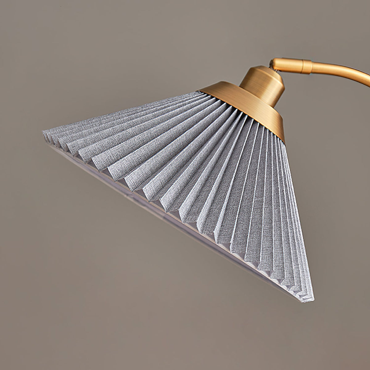 The grey pleated shade of this Clérachic floor lamp, with its brass collar and the start of the curved brass arm.