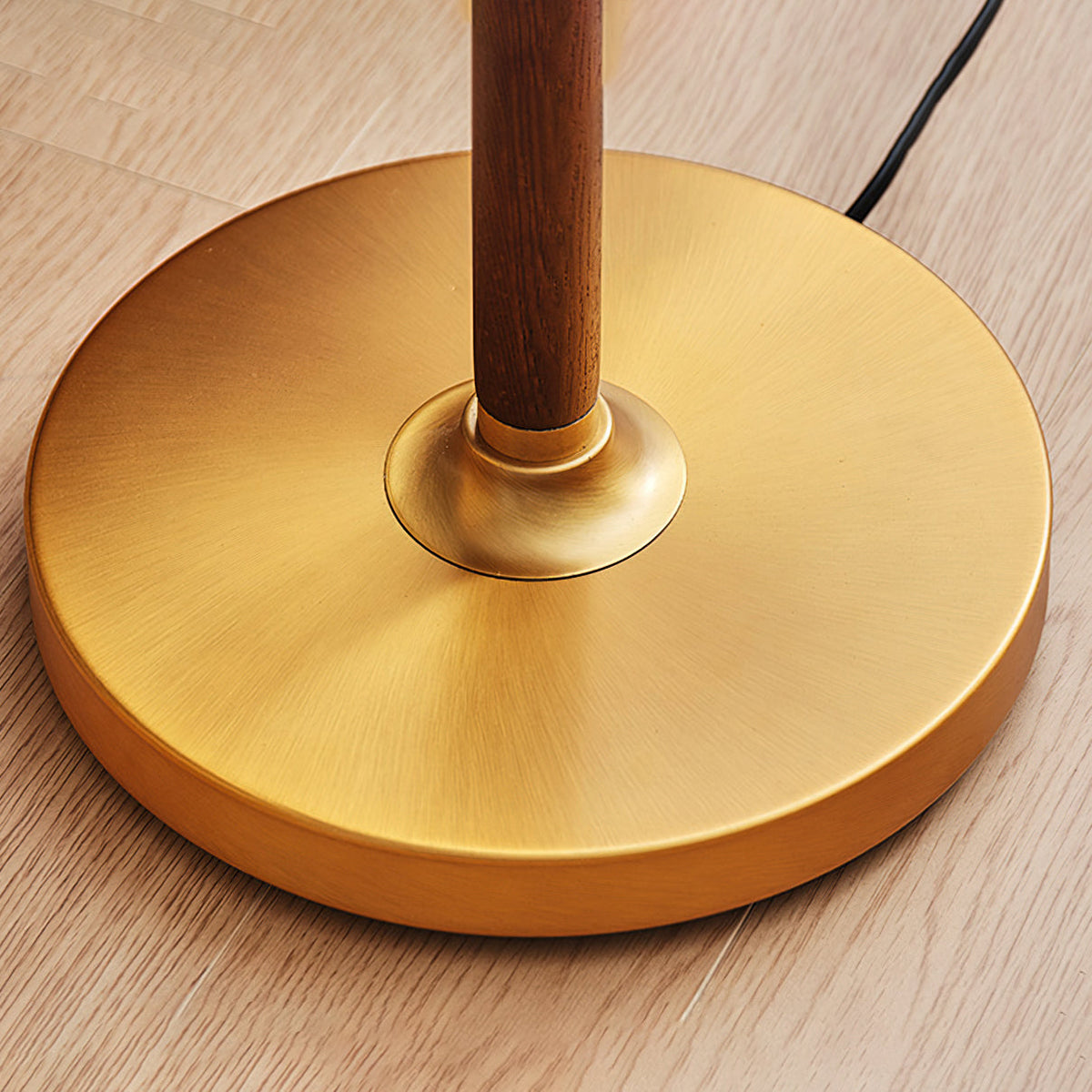 Close view of the round brushed brass base of this Clérachic floor lamp, with the walnut stem rising from a brass collar.