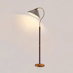 Clérachic floor lamp with a grey pleated shade, a curved brass arm and a walnut stem, throwing a warm pool of light on a pale wall.