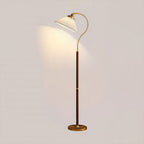 A Clérachic floor lamp with a white pleated shade, curved brass arm, walnut stem and brass base, lit against a pale wall.