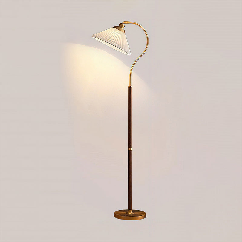 A Clérachic floor lamp with a white pleated shade, curved brass arm, walnut stem and brass base, lit against a pale wall.