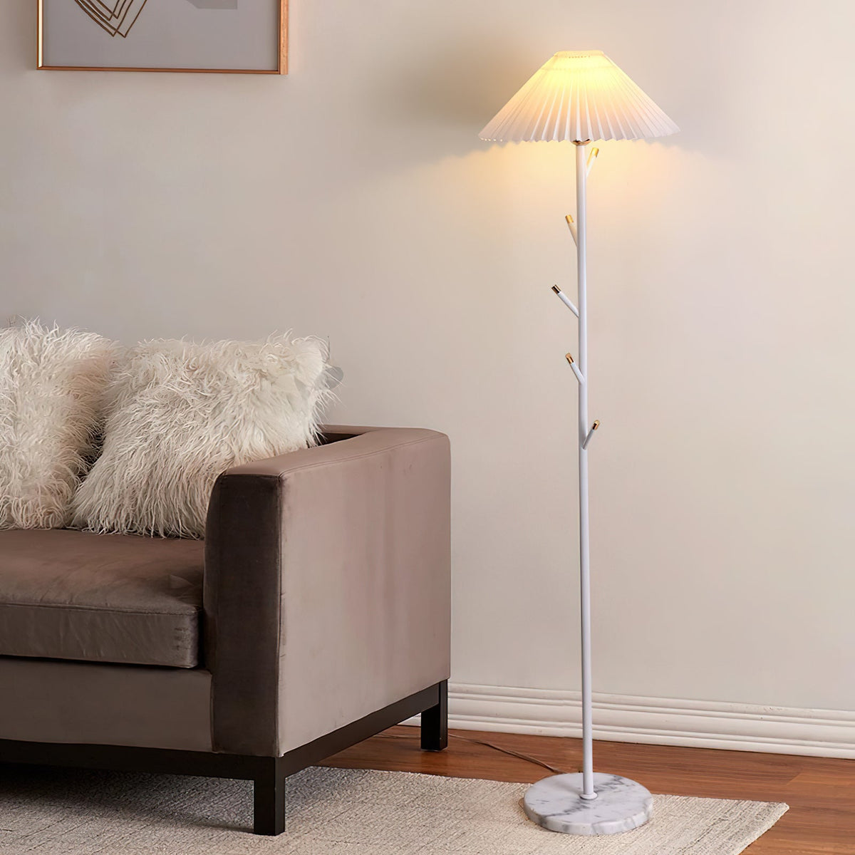 Clérachic floor lamp in white with a pleated shade, lit beside a taupe sofa with fluffy cushions on a woven rug.