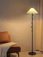 Black Clérachic floor lamp lit in a warm corner, with a knitted throw draped over a tan leather chair beside it.