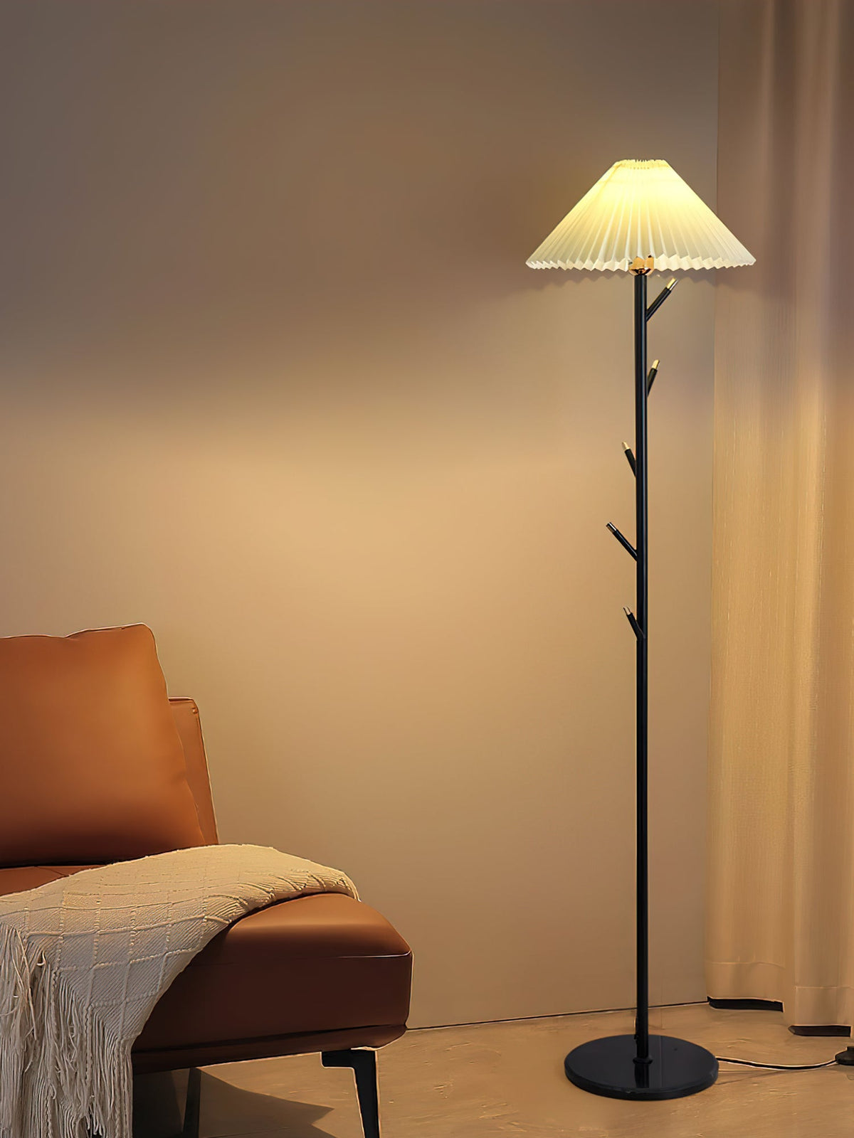 Black Clérachic floor lamp lit in a warm corner, with a knitted throw draped over a tan leather chair beside it.