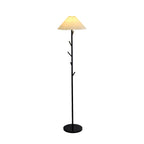 Black Clérachic floor lamp, lit, with a pleated shade, slim pole with branch hooks and a dark round base on a white backdrop.