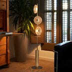 This Clérachic floor lamp glows beside a tall potted palm and shuttered window, with a wooden desk and black leather chair nearby.