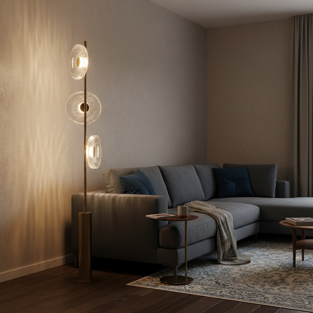 A Clérachic floor lamp beside a grey sofa in a warm room, its glass discs glowing and casting light patterns on the wall.