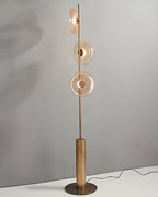 Tall Clérachic floor lamp on a round bronze foot against a grey wall, its glass discs tinted amber and its cord trailing away.