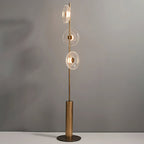 Full view of this Clérachic floor lamp on its round bronze foot against a soft grey wall, with three glass discs lit.
