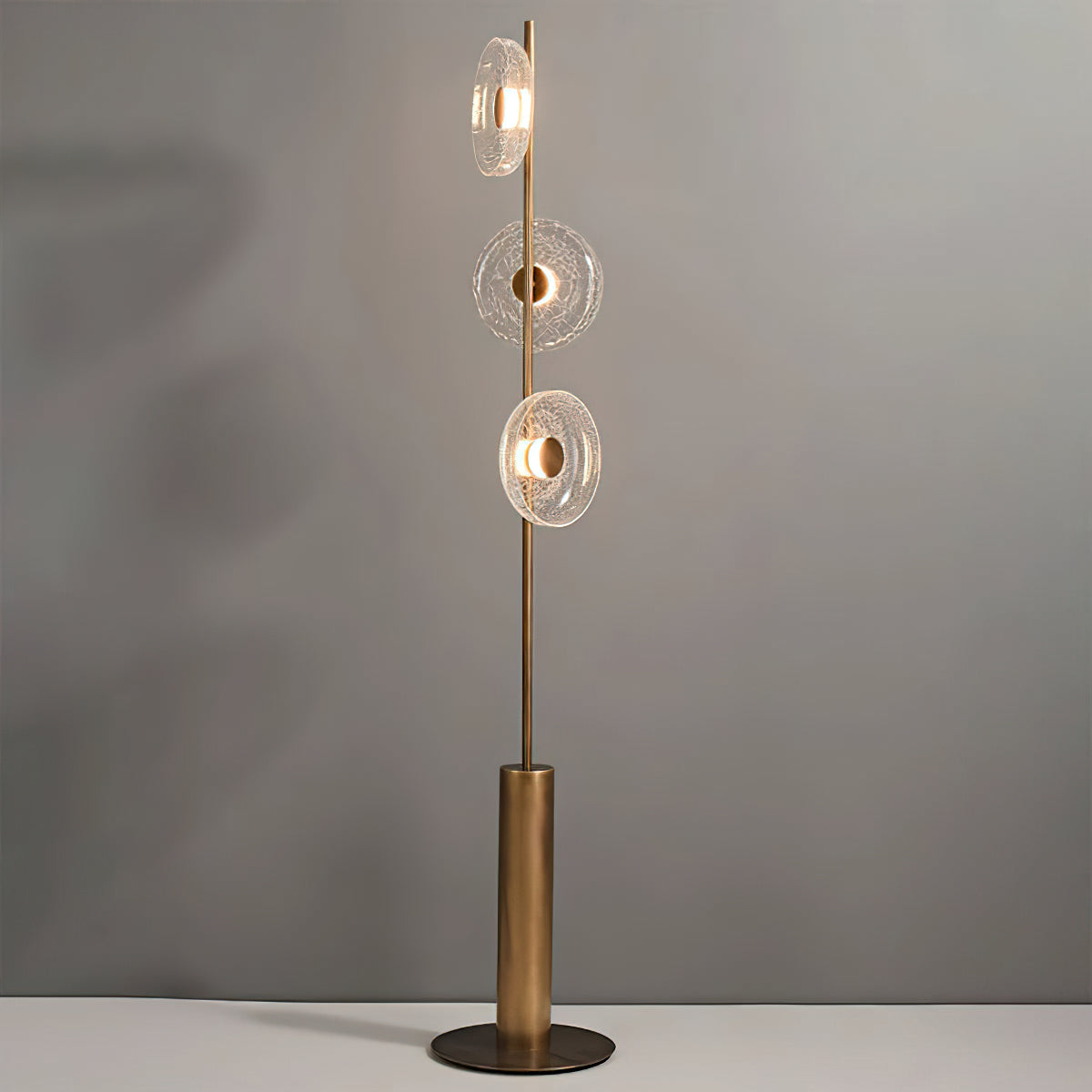 Full view of this Clérachic floor lamp on its round bronze foot against a soft grey wall, with three glass discs lit.