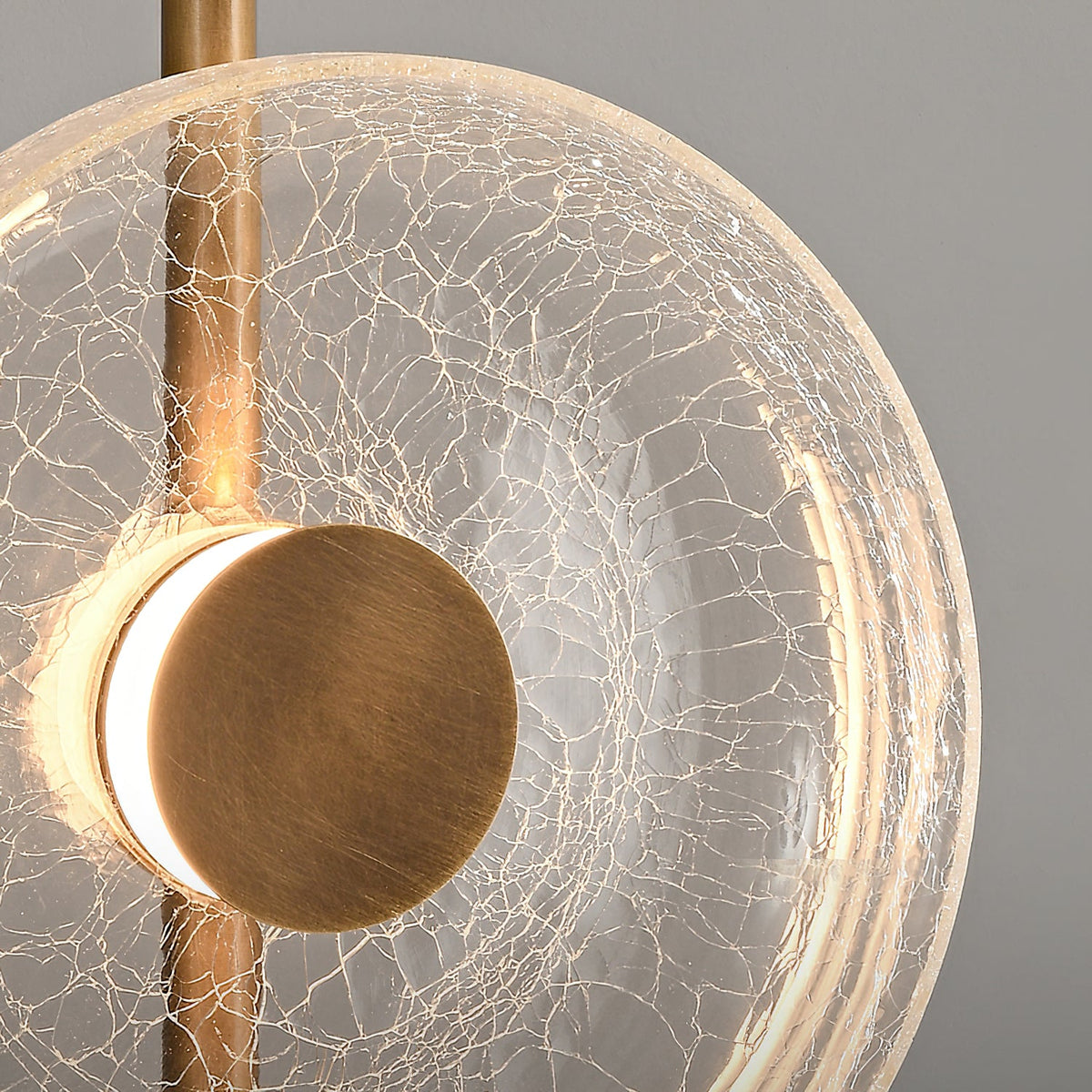 Close view of the cracked glass disc, brass-toned centre cap and stem on this Clérachic floor lamp, with light glowing behind it.