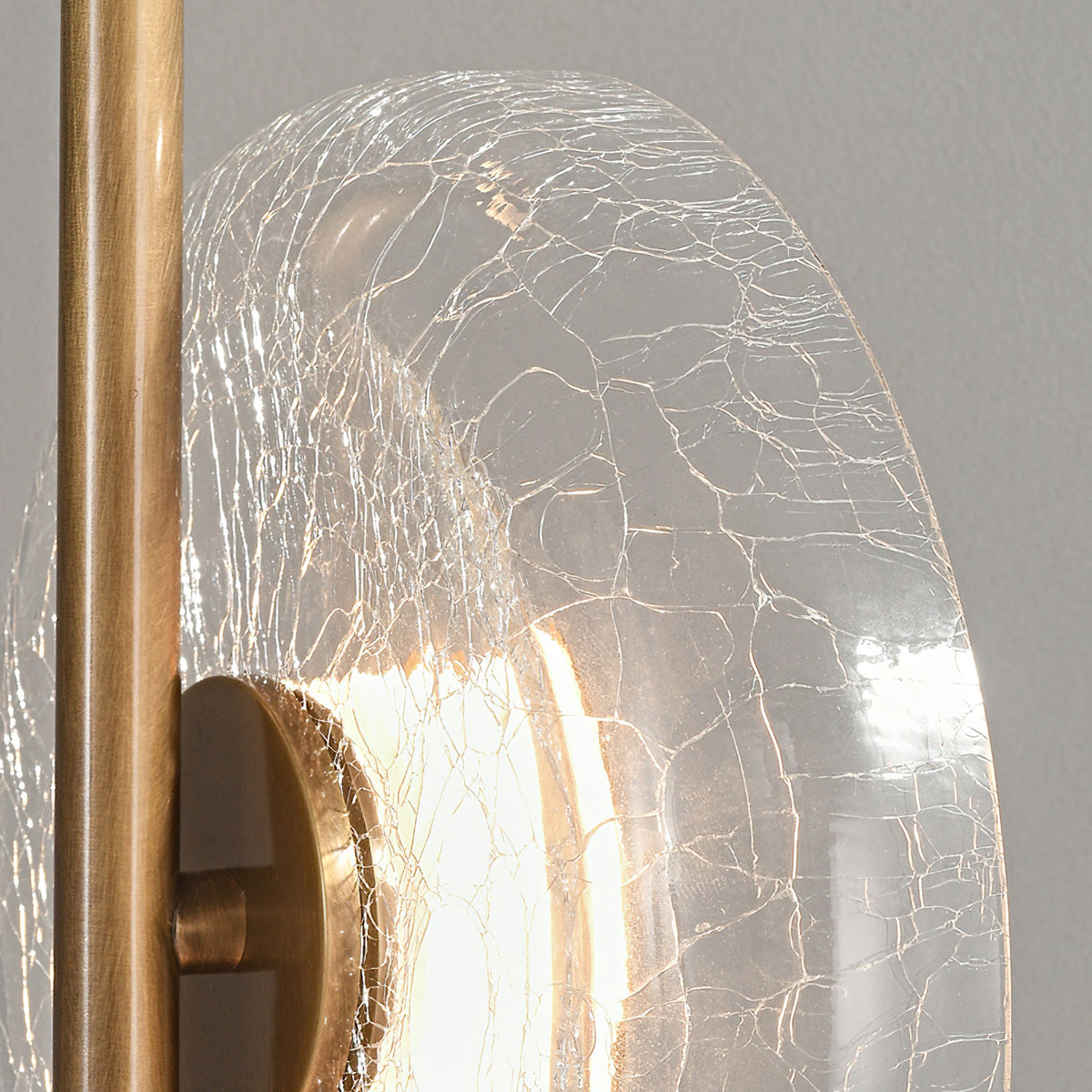 Close view of the veined, cracked glass disc and bronze stem on this Clérachic floor lamp, with a bright light behind the cap.