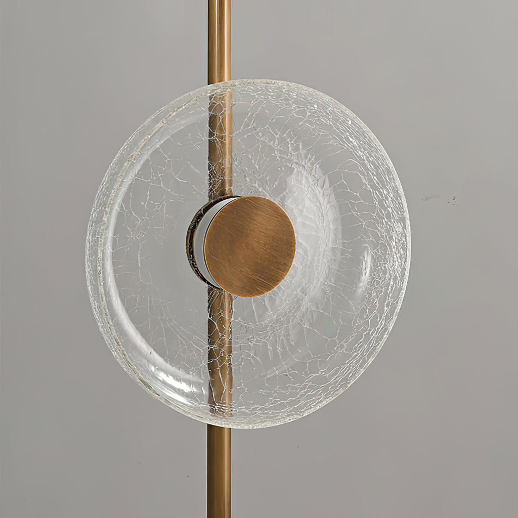 Front view of one clear cracked glass disc with a bronze centre cap, mounted on the slim stem of this Clérachic floor lamp.