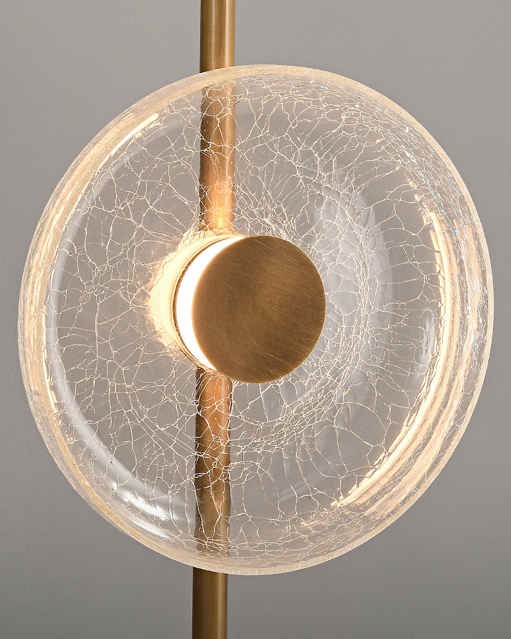 Close view of a lit cracked glass disc with a warm glow around its bronze centre cap, on this Clérachic floor lamp.
