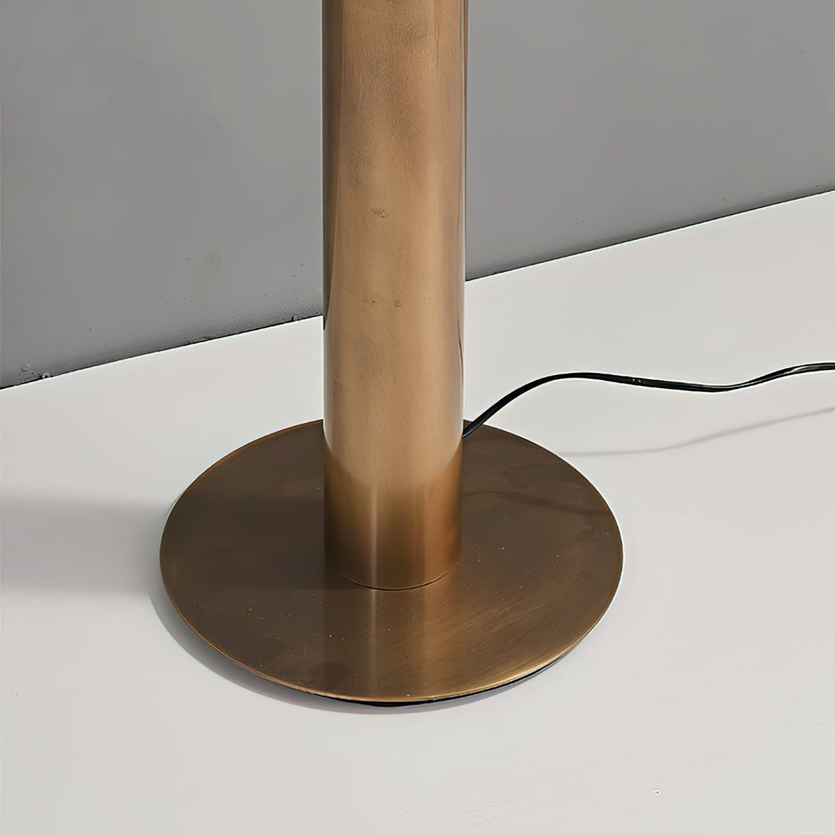 Close view of the round bronze foot and the bottom of the cylinder base on this Clérachic floor lamp, with the cord running off.