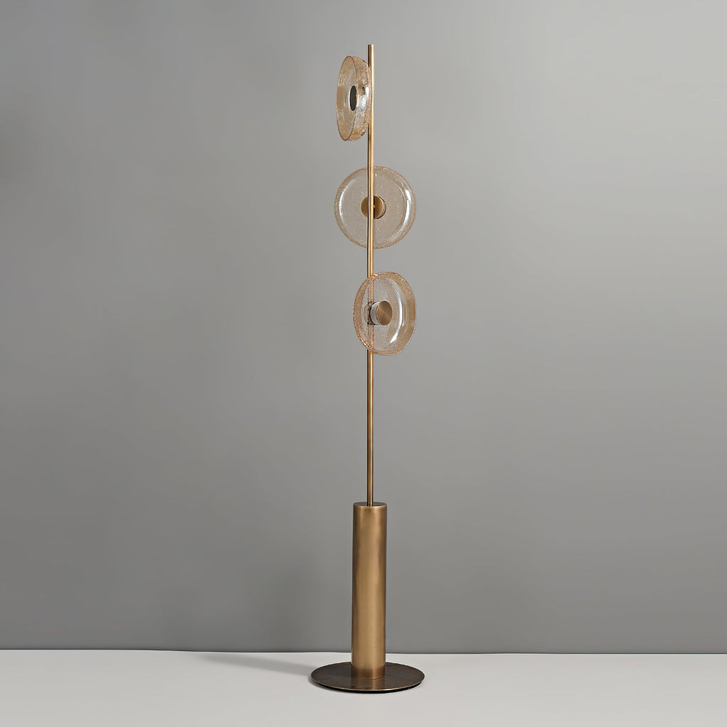 Clérachic floor lamp, unlit, against a grey wall, with three amber-tinted glass discs on a slim stem above a bronze base.