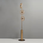 Clérachic floor lamp, unlit, against a grey wall, with three amber-tinted glass discs on a slim stem above a bronze base.