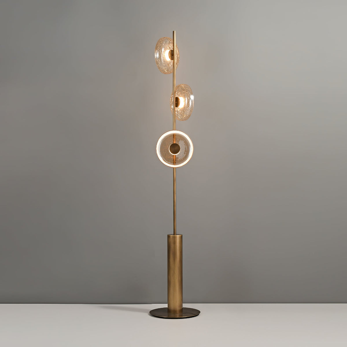 This Clérachic floor lamp switched on, with the lowest disc lit as a bright ring and the upper two glowing amber.